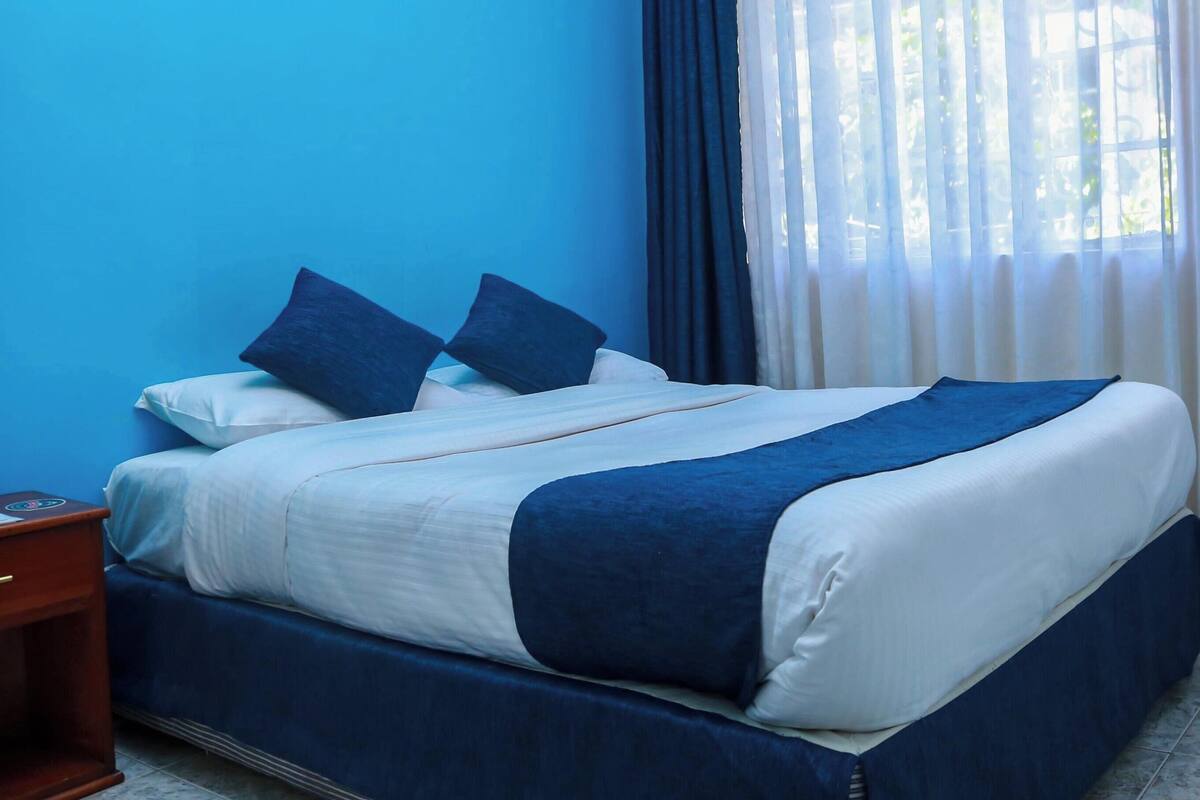 A bed with a blue and white bedspread, two pillows, and a wooden nightstand.
