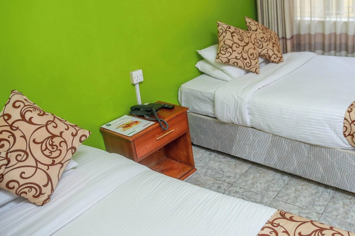 A hotel room with two beds, a nightstand with a phone, and a green wall.