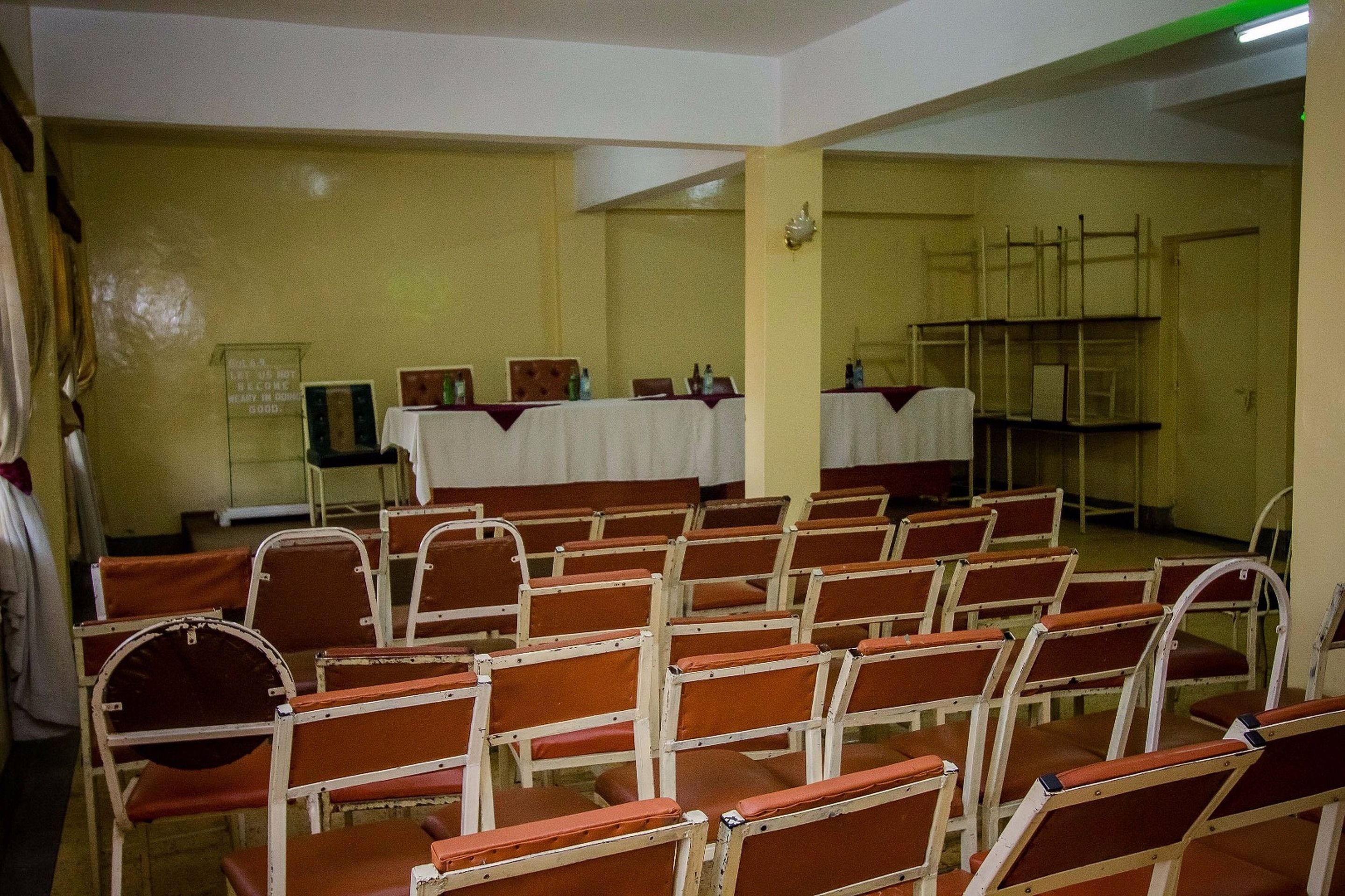 Une salle de conférence avec des rangées de chaises et de tables, un tableau blanc et un panneau affiché sur le mur.