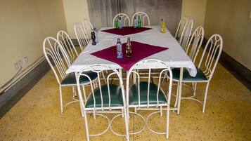 Una mesa de comedor con estructura metálica blanca y sillas con reposabrazos verdes, dispuesta con botellas de agua y una gaseosa.