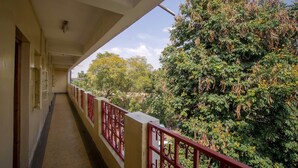 Un couloir orné d’une rambarde rouge, qui mène à un balcon offrant une vue sur un feuillage dense et des arbres.