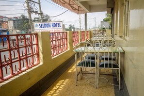A hotel balcony with metal chairs and tables, a sign for Seldoom Hotel, and a view of buildings in the background. - Seldom Hotel (Nairobi)