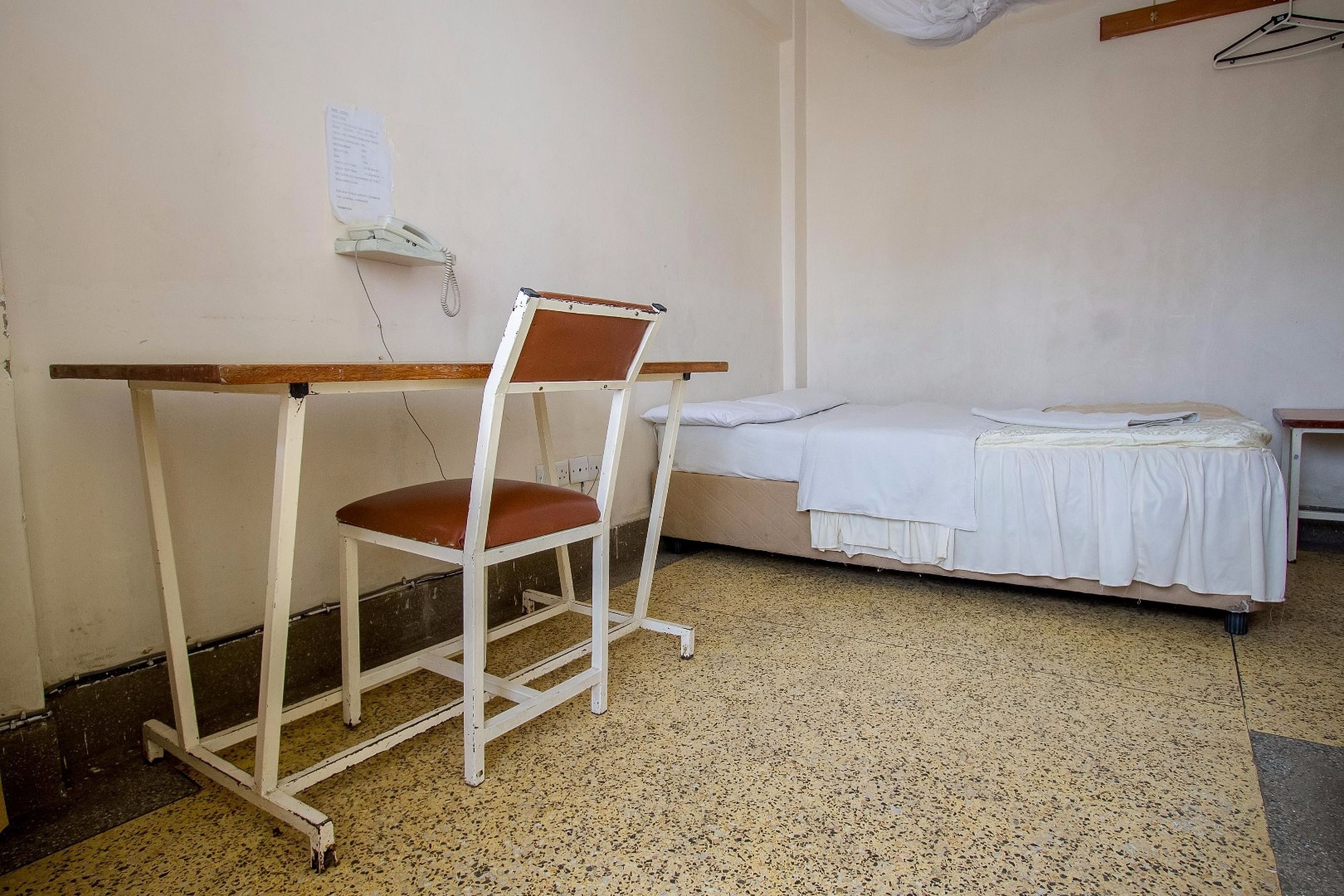Een kamer met een bed, een bureau met stoel, en een telefoon aan de muur.