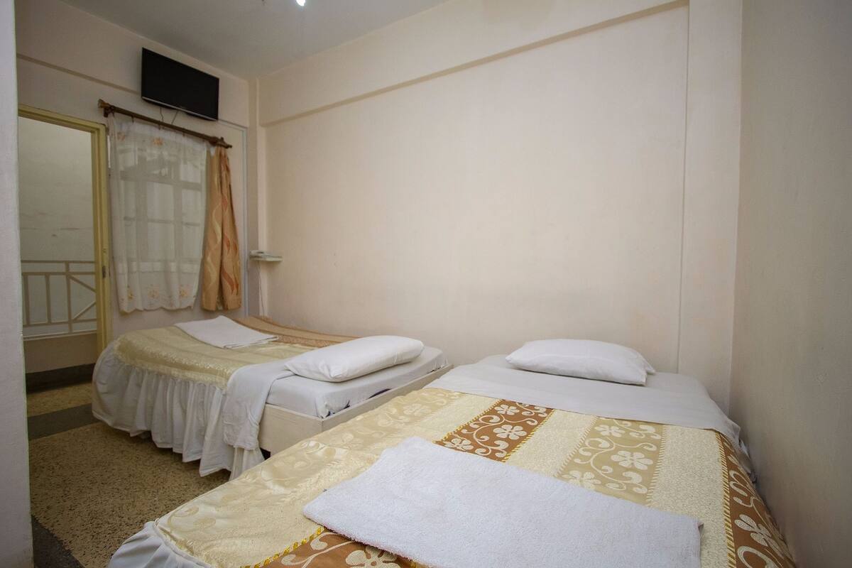 A hotel room with two beds, a television mounted on the wall, and a window with curtains.