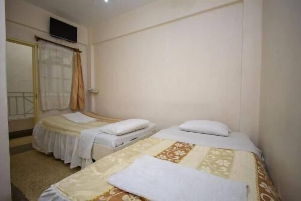A room with two beds, a window with curtains, and a door with a mirror.