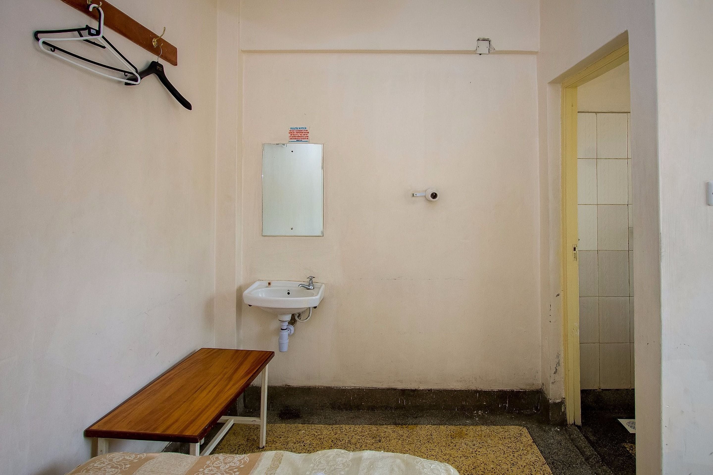 Une petite pièce simple, avec un banc en bois, un lavabo blanc et une porte donnant sur une autre pièce.