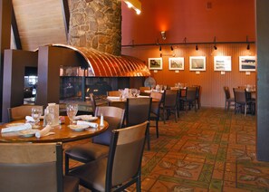 Un restaurante con paredes de madera, un pilar de piedra y una alfombra estampada. Las mesas están preparadas con platos, vasos y cubiertos.