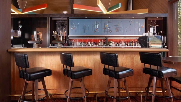 Una zona de bar con mostrador, taburetes y una variedad de botellas.