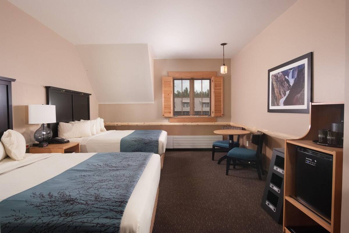 Ein Hotelzimmer mit zwei Betten, einem Schreibtisch, einem Sessel, einem Fernseher und einem Fenster mit Rollläden.