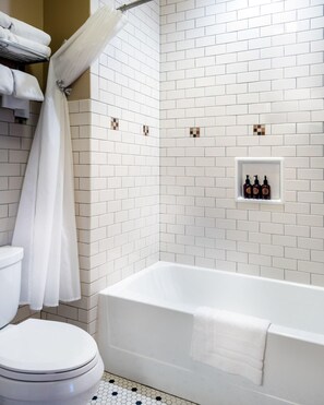 A bathroom with white subway tiles, a white bathtub, a toilet, and a shower curtain.