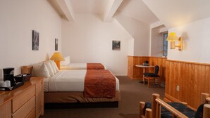 Habitación de hotel con dos camas, un escritorio de madera, una silla, una mesita y una lámpara.