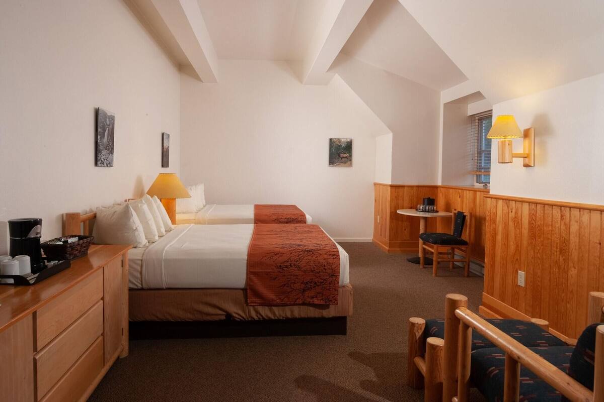 Ein Hotelzimmer mit zwei Betten, einem Holztisch, einem Stuhl, einem kleinen Tisch und einer Lampe.