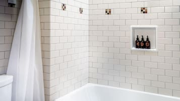 A bathroom with white subway tiles, a white bathtub, a toilet, and a shower curtain.