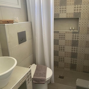 A bathroom with a toilet, a sink, and a shower area. - Hotel Pelagos (Amorgos)