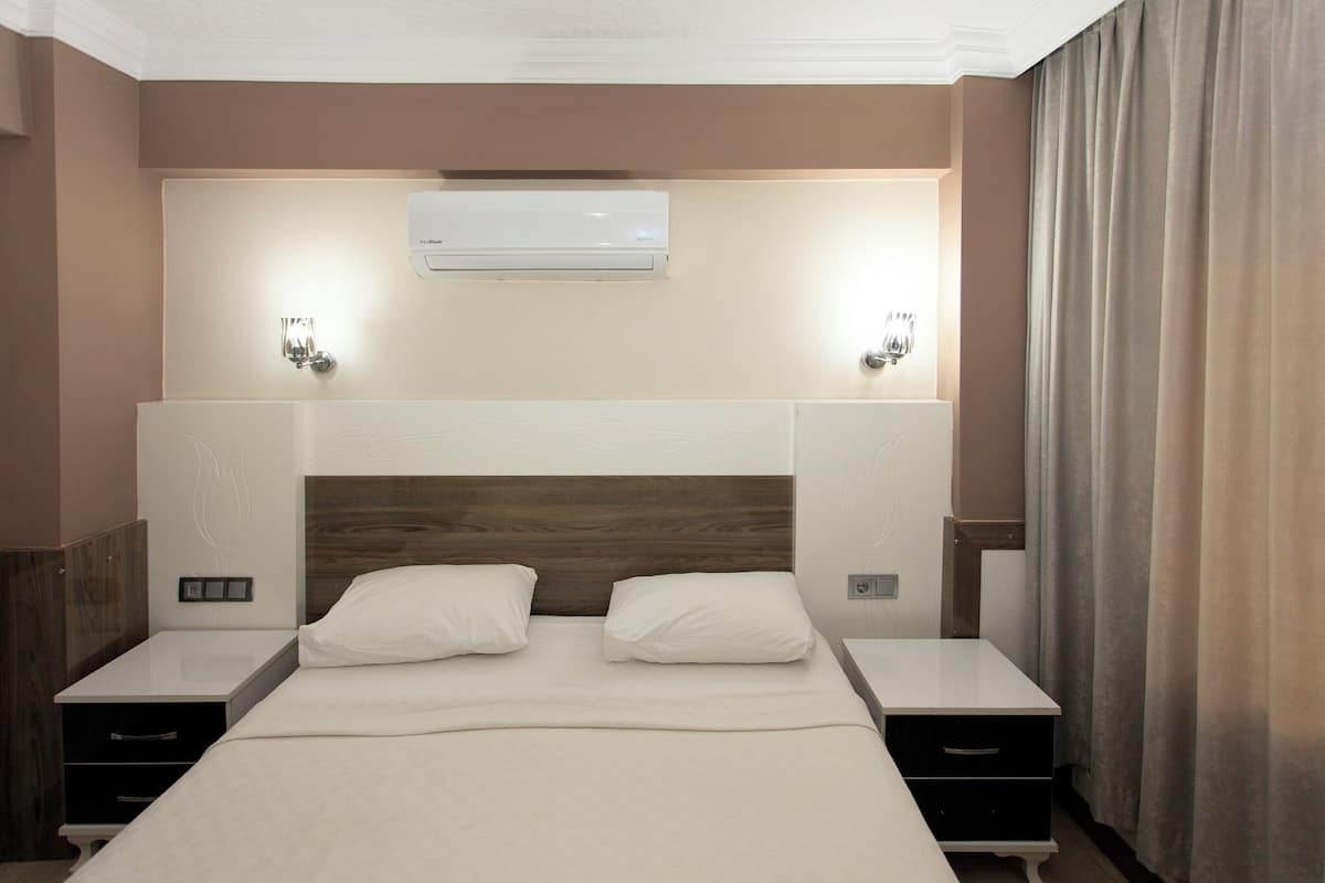 Ein Hotelzimmer mit einem großen Bett, zwei Nachttischen, einer Wandklimaanlage und zwei Wandleuchten.