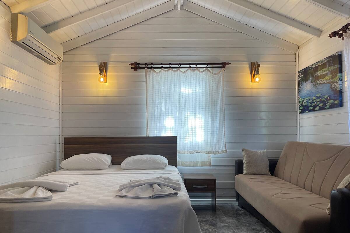 A bedroom with a bed, a sofa, a window with curtains, and wall-mounted lights.