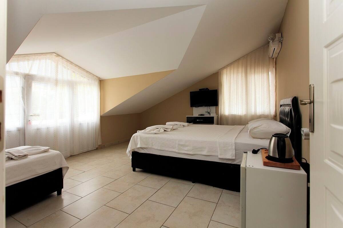 A bedroom with a bed, a bedside table with a kettle, a TV, and a heater.