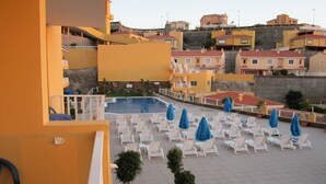 Un espace piscine aménagé sur le toit, avec des chaises longues blanches et des parasols bleus, entouré d’immeubles aux toits rouges.