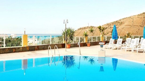 Une piscine à l’eau d’un bleu cristallin, entourée de chaises longues et de plantes en pot, offrant une vue sur un paysage côtier.