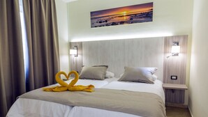Une chambre d’hôtel comprenant un lit, deux tables de chevet, une petite table, un tableau représentant un coucher de soleil et une décoration en forme de cœur faite avec une serviette.