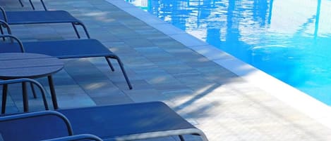 A swimming pool with lounge chairs and a covered area.