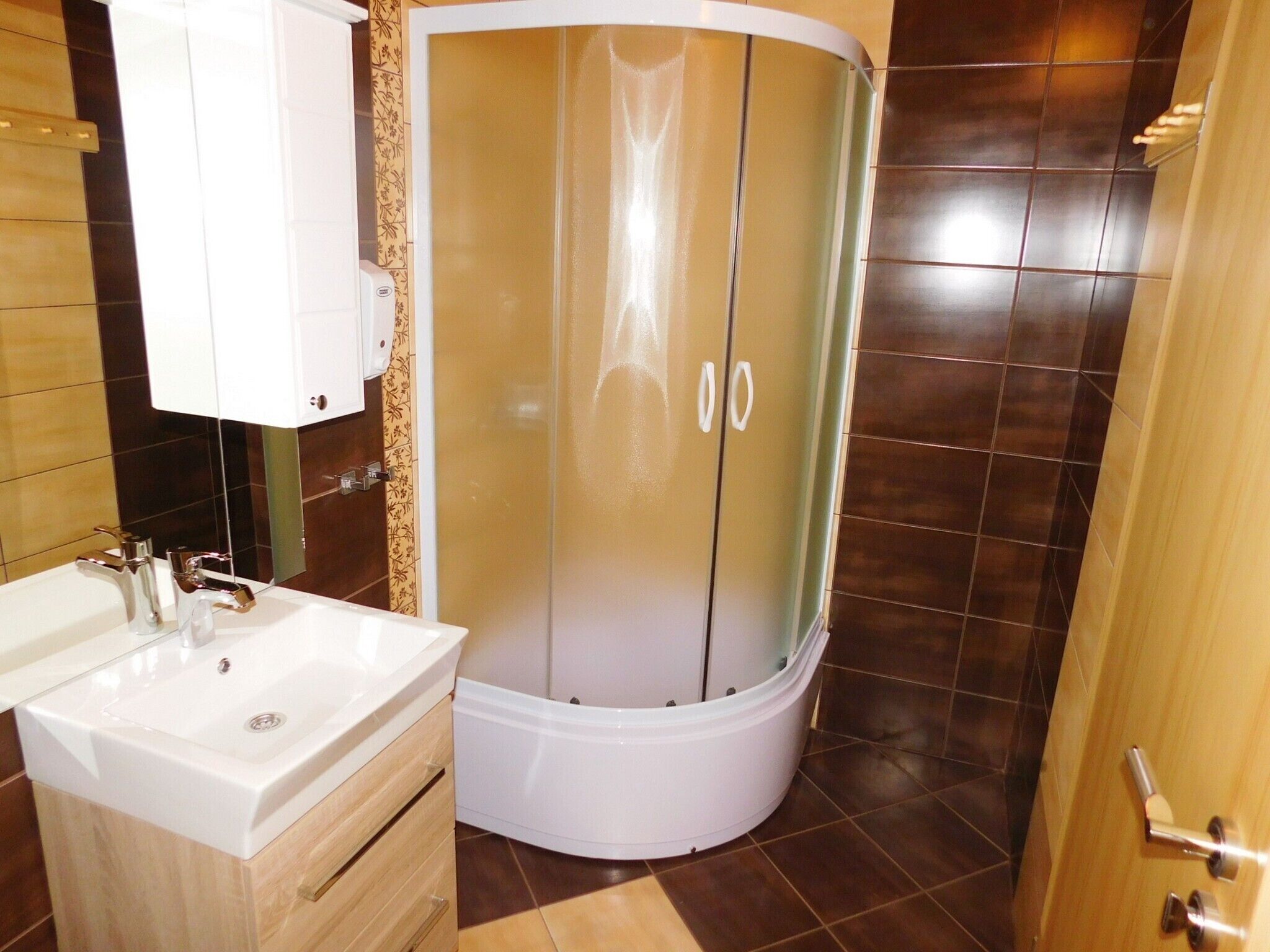 A bathroom with a white sink, a shower enclosure, and a wooden cabinet.