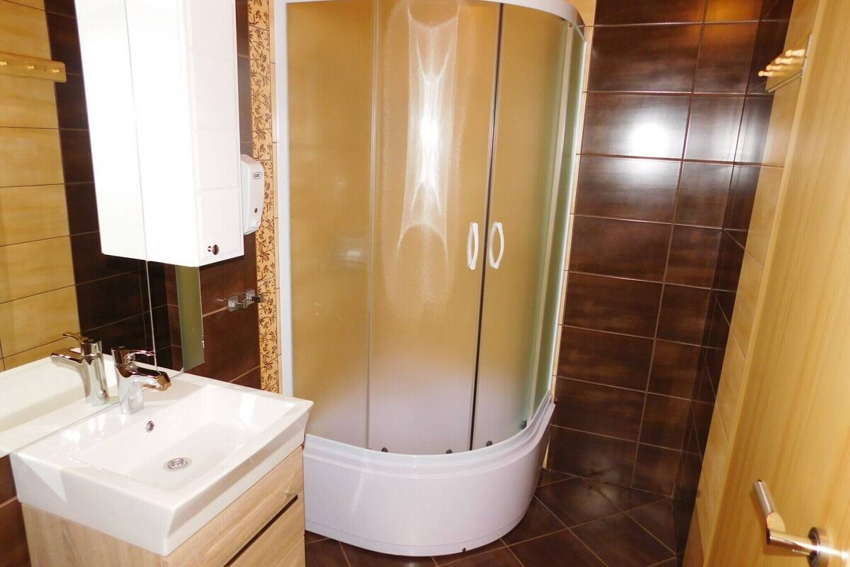 A bathroom with a white sink, a shower enclosure, and a wooden cabinet.