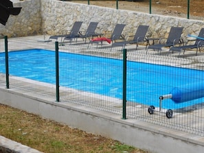 A swimming pool with a stone wall, green fence, and lounge chairs. - House Sara 2 (Rakovica)