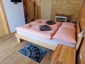 A wooden bed with a pink blanket and pillows, a small wooden table, a patterned rug, and a wooden wall. - House Sara 2 (Rakovica)
