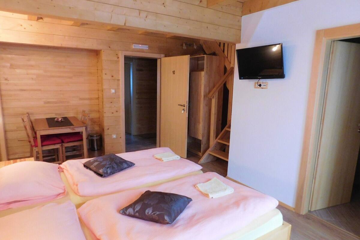 Une chambre dans un chalet en bois, avec deux lits, une télévision et un escalier.