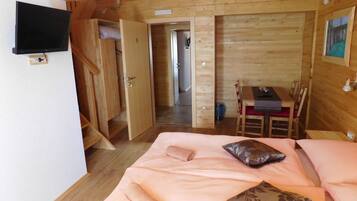 A wooden cabin room with a bed, a TV, a dining table, and a chair.
