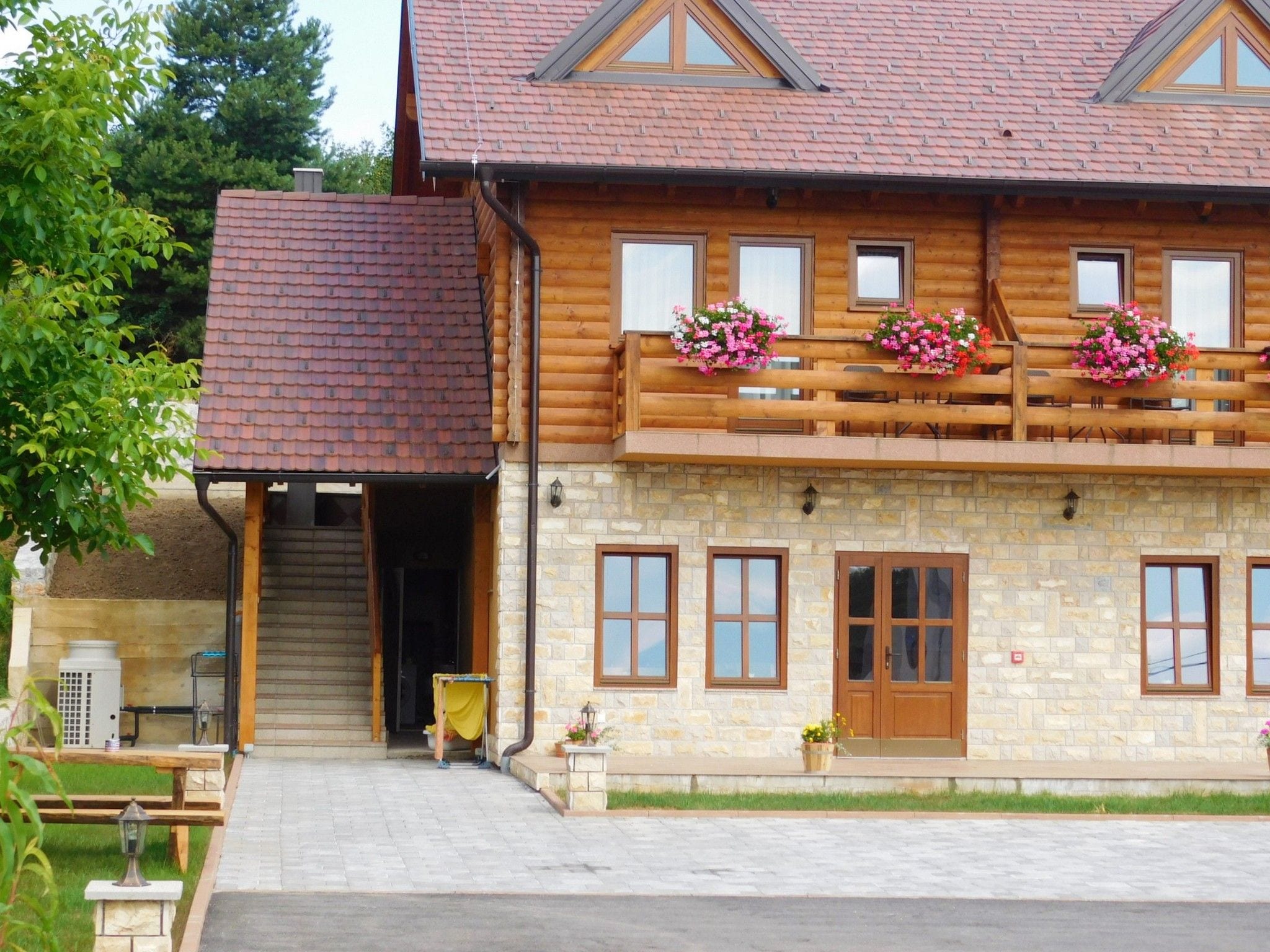 Ein zweistöckiges Holzhaus mit Steinverkleidung, zahlreichen Fenstern und Blumenkästen am Balkon.