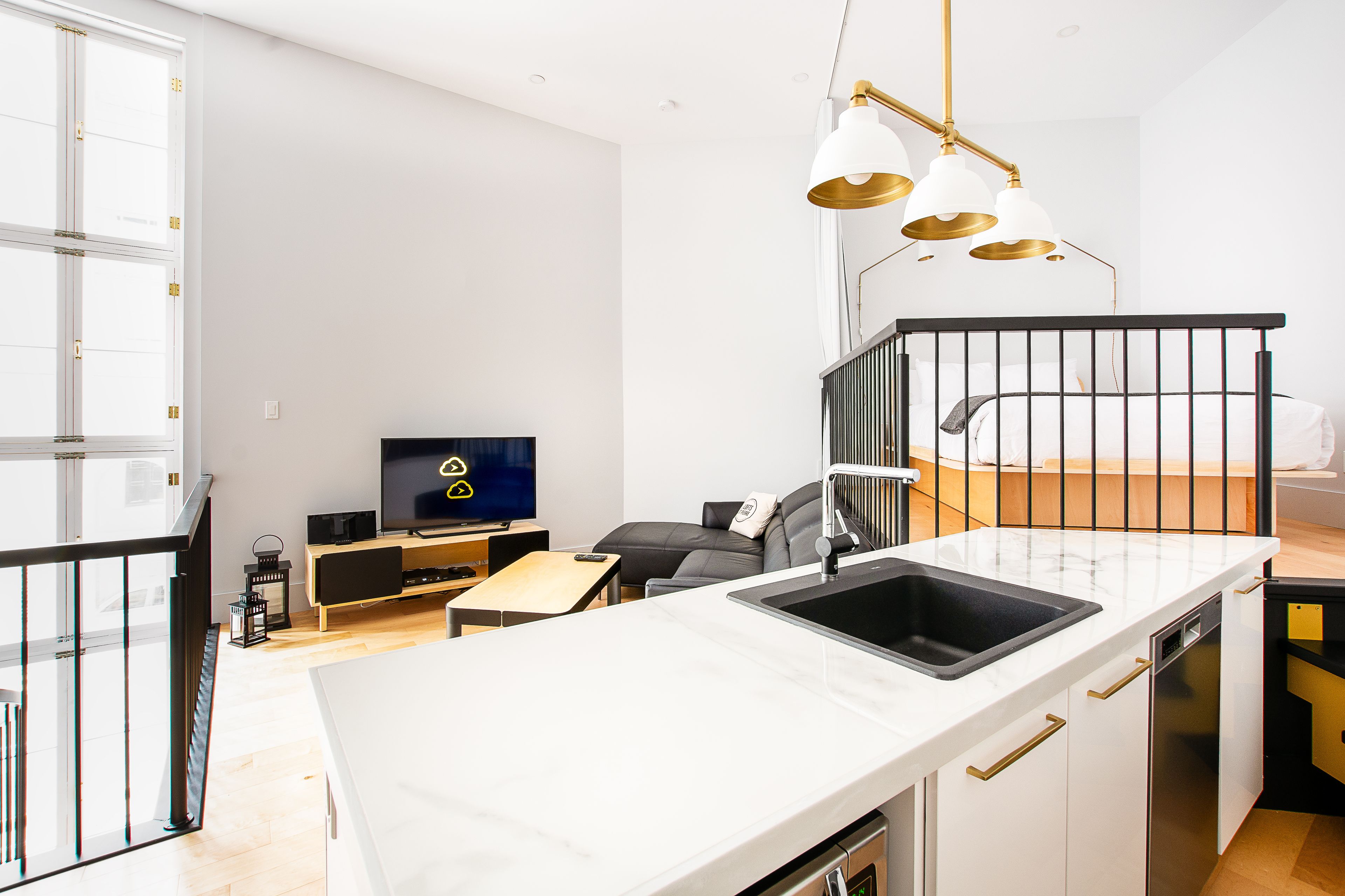 A modern kitchen with a white countertop, black sink, and gold pendant lights.