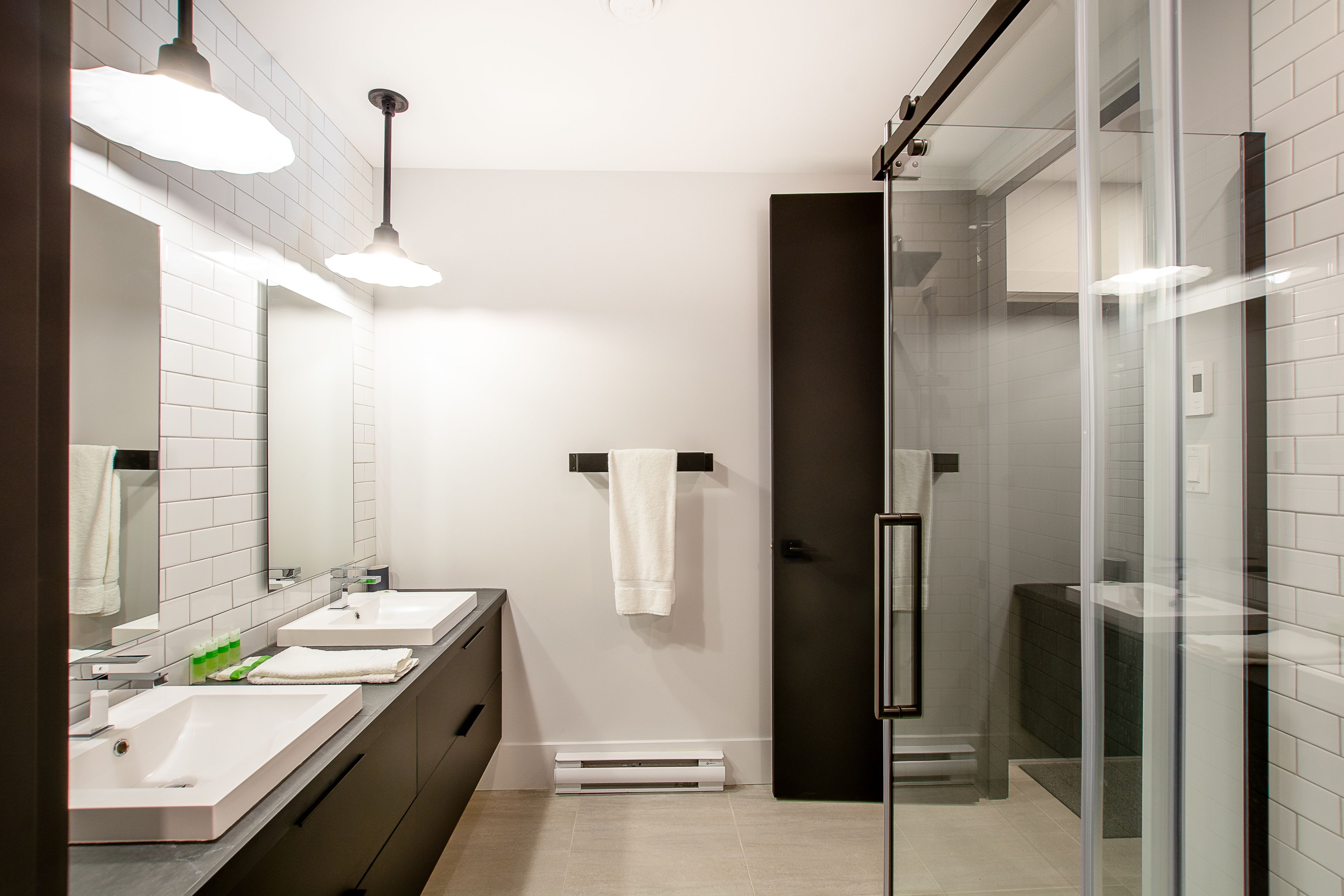 Une salle de bain moderne avec deux lavabos, une douche en verre et un porte-serviettes.