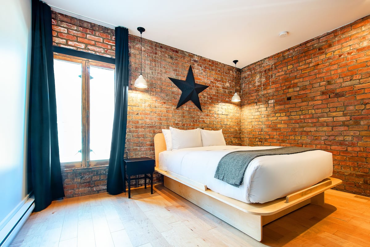 A modern bedroom with a brick wall, a star decoration, a bed with white bedding, and a desk with a chair.