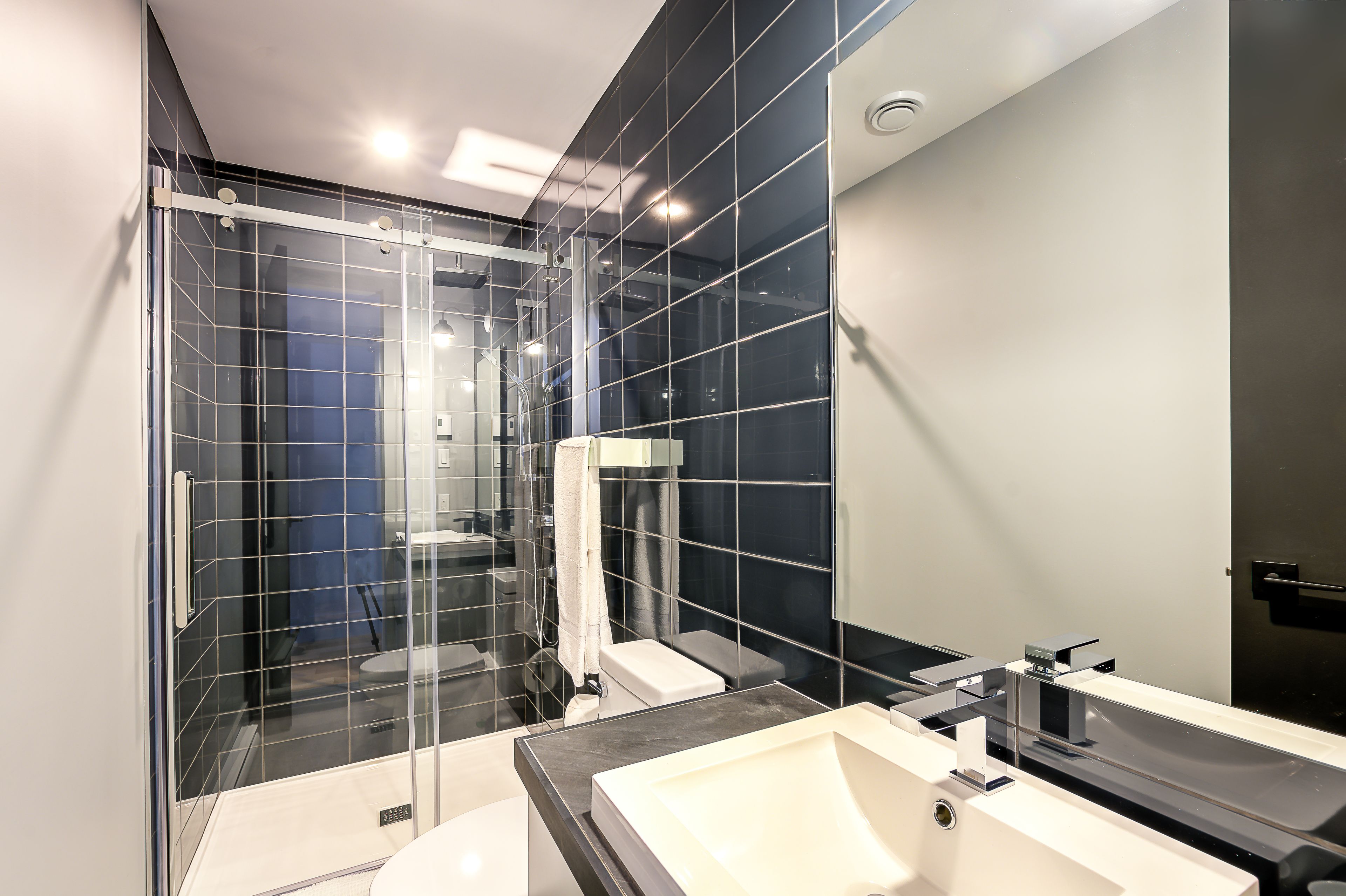 Une salle de bain moderne avec une douche à parois de verre, un lavabo blanc et un grand miroir.