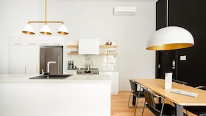 A modern kitchen with a central island, white cabinetry, a stainless steel refrigerator, and a dining area with a wooden table and chairs.