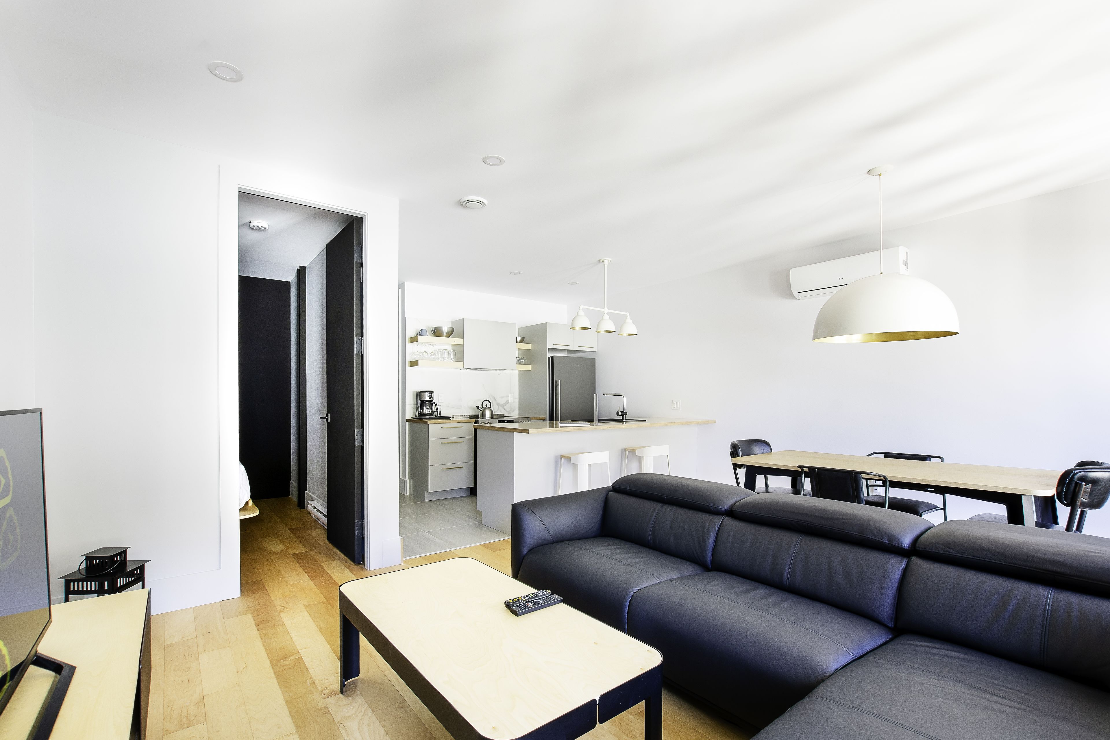 A modern living room with a black leather sofa, a wooden coffee table, and a white pendant light.