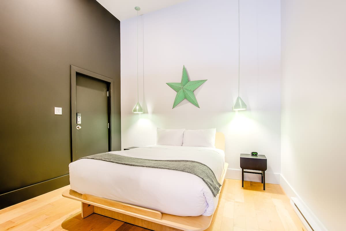 A neatly made bed with a wooden frame, a bedside table with a green object, and a green star decoration on the wall.