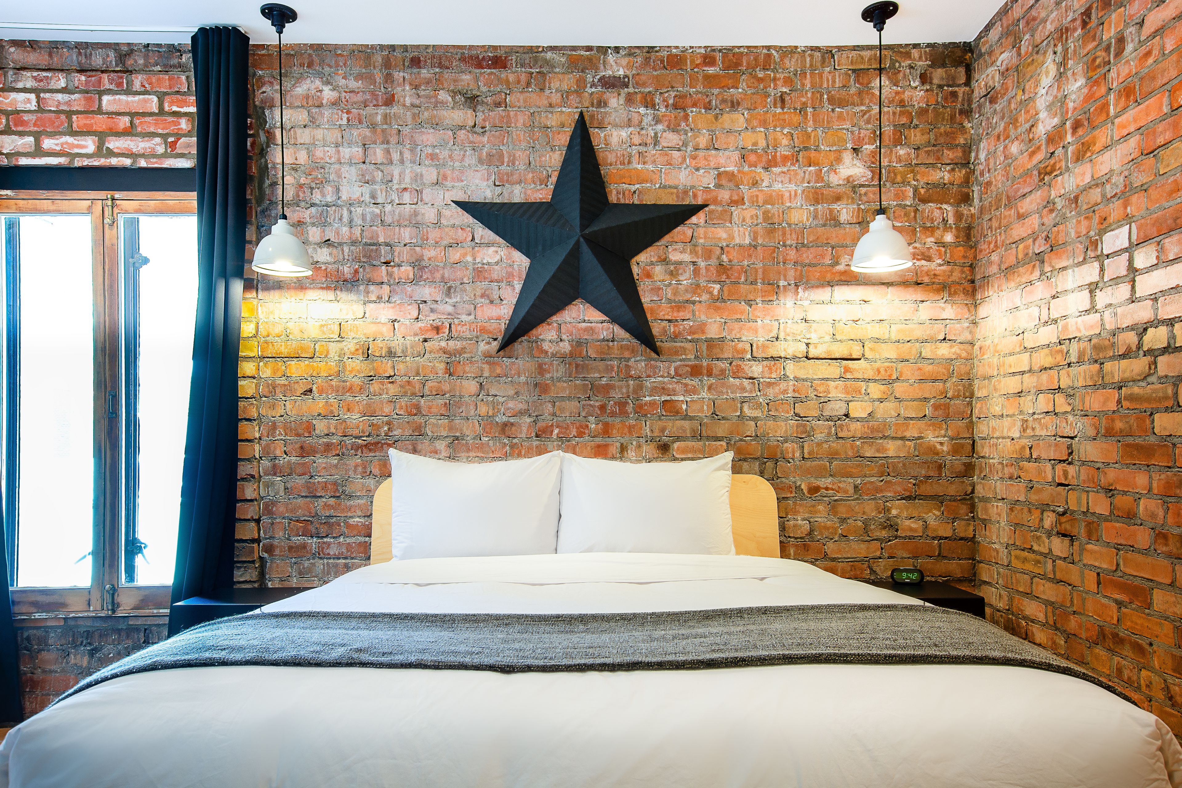 A bed in a room with a brick wall, a star decoration, and two pendant lights.