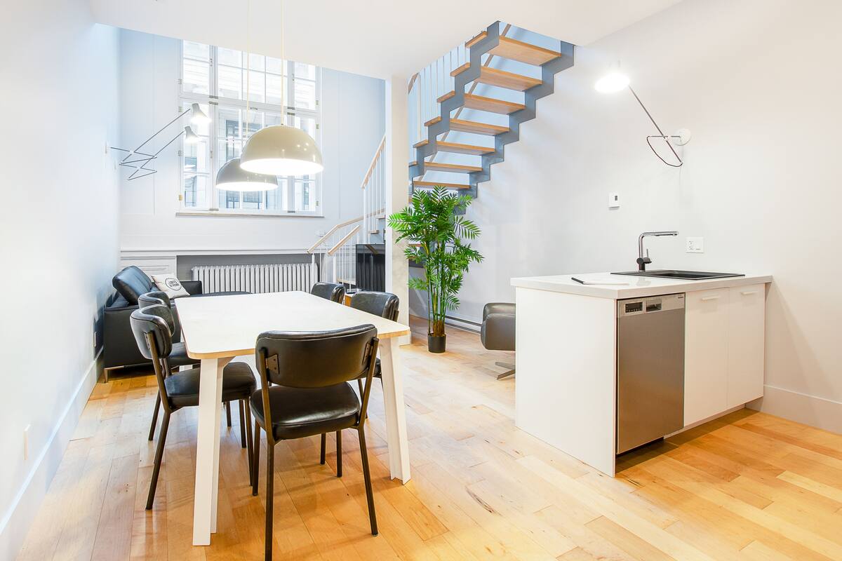 A modern kitchen with a white countertop, a built-in dishwasher, and a wooden staircase.