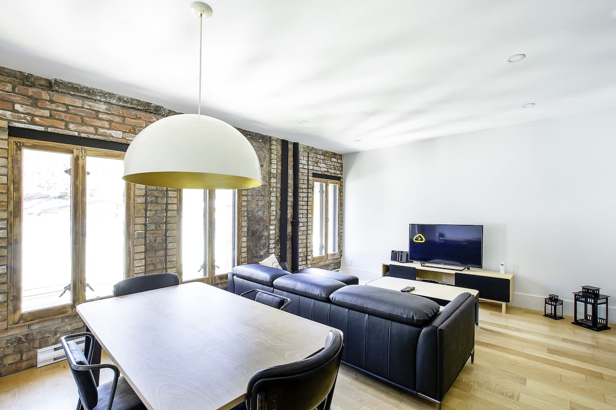 A modern living room with a dining area, a sofa, a TV, and large windows.