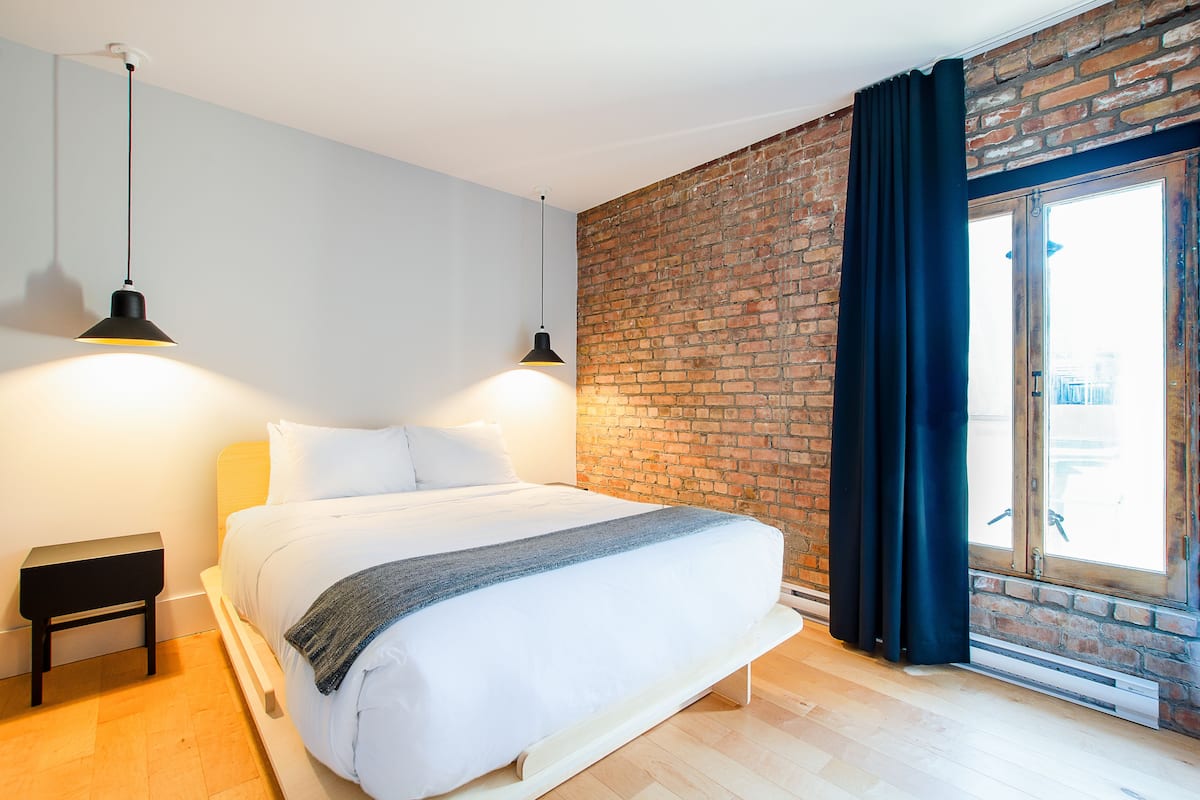 A modern bedroom with a brick wall, a large bed, and two pendant lights.