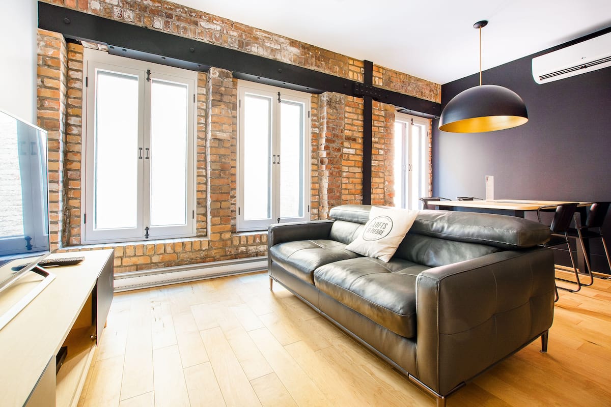 A modern living room with a leather sofa, a wooden desk, and a large window with a view of the outdoors.