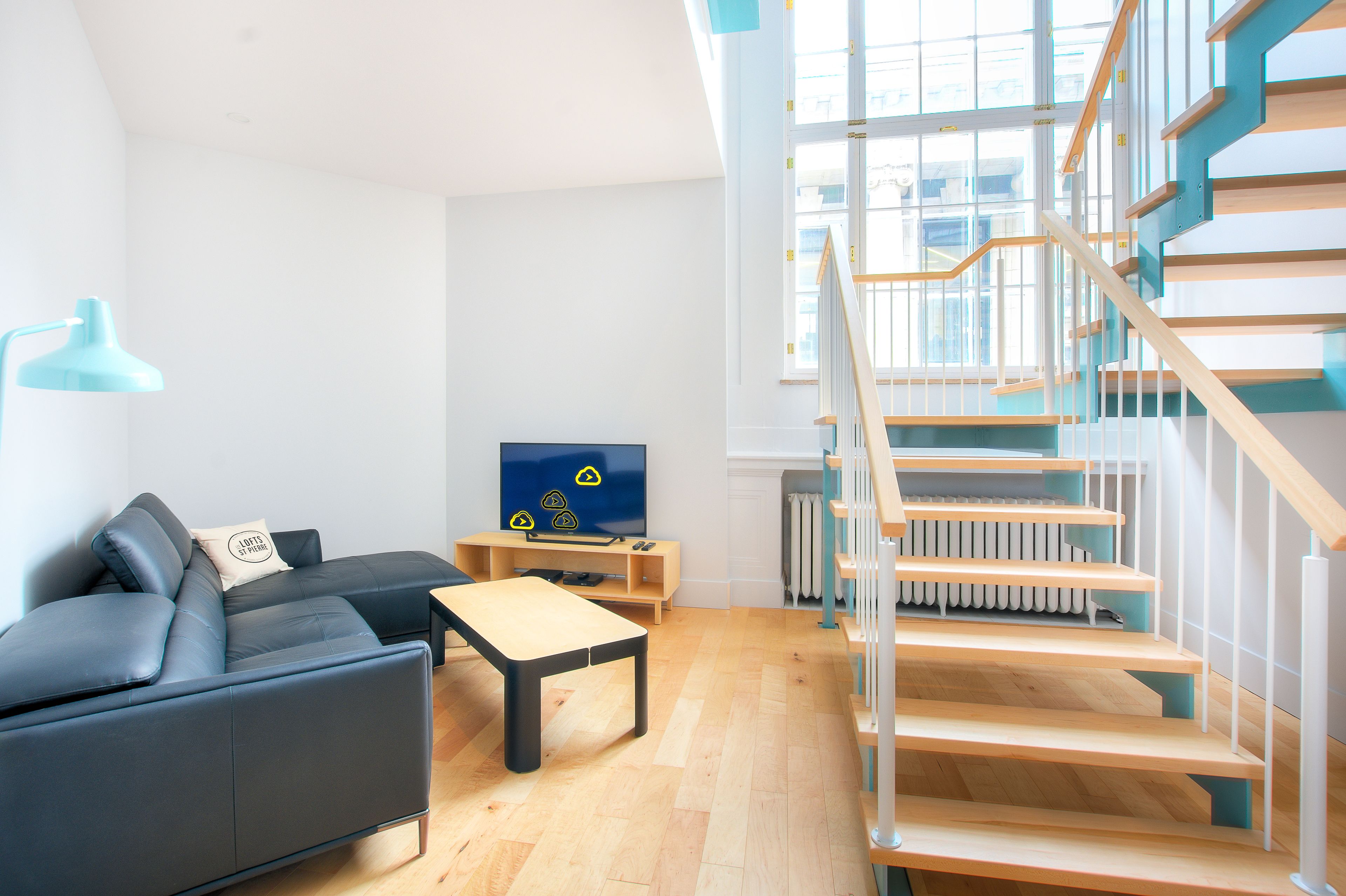 A modern living room with a sofa, a coffee table, a TV, and a staircase with wooden steps and white railings.