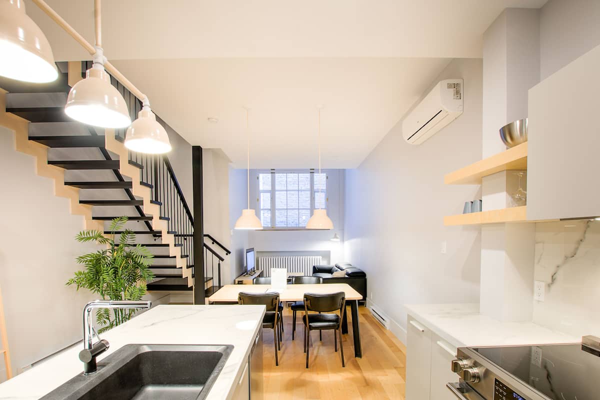 A modern kitchen with a dining area, a staircase, and a built-in air conditioning unit.