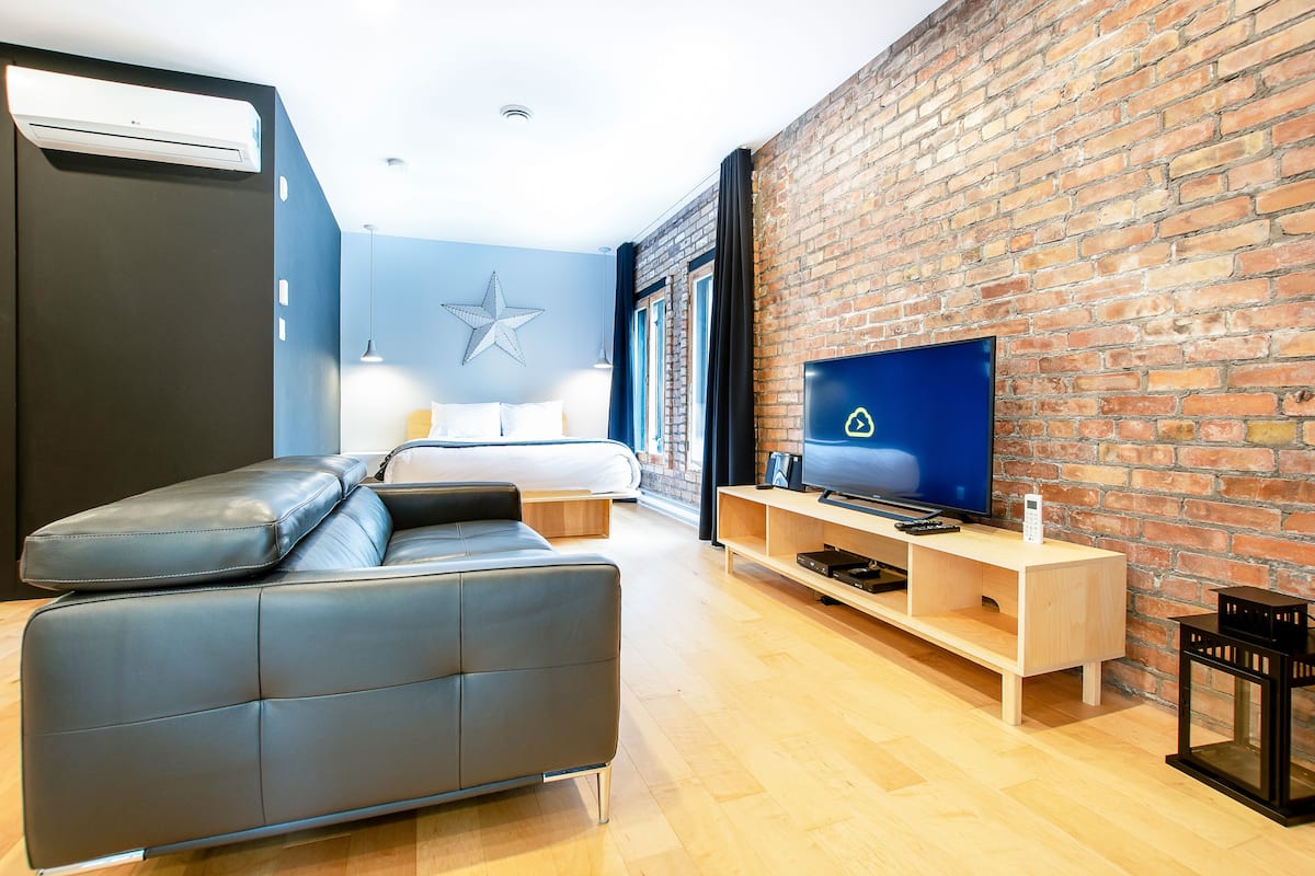A modern room with a brick wall, a flat-screen TV, a sofa, and a bed.