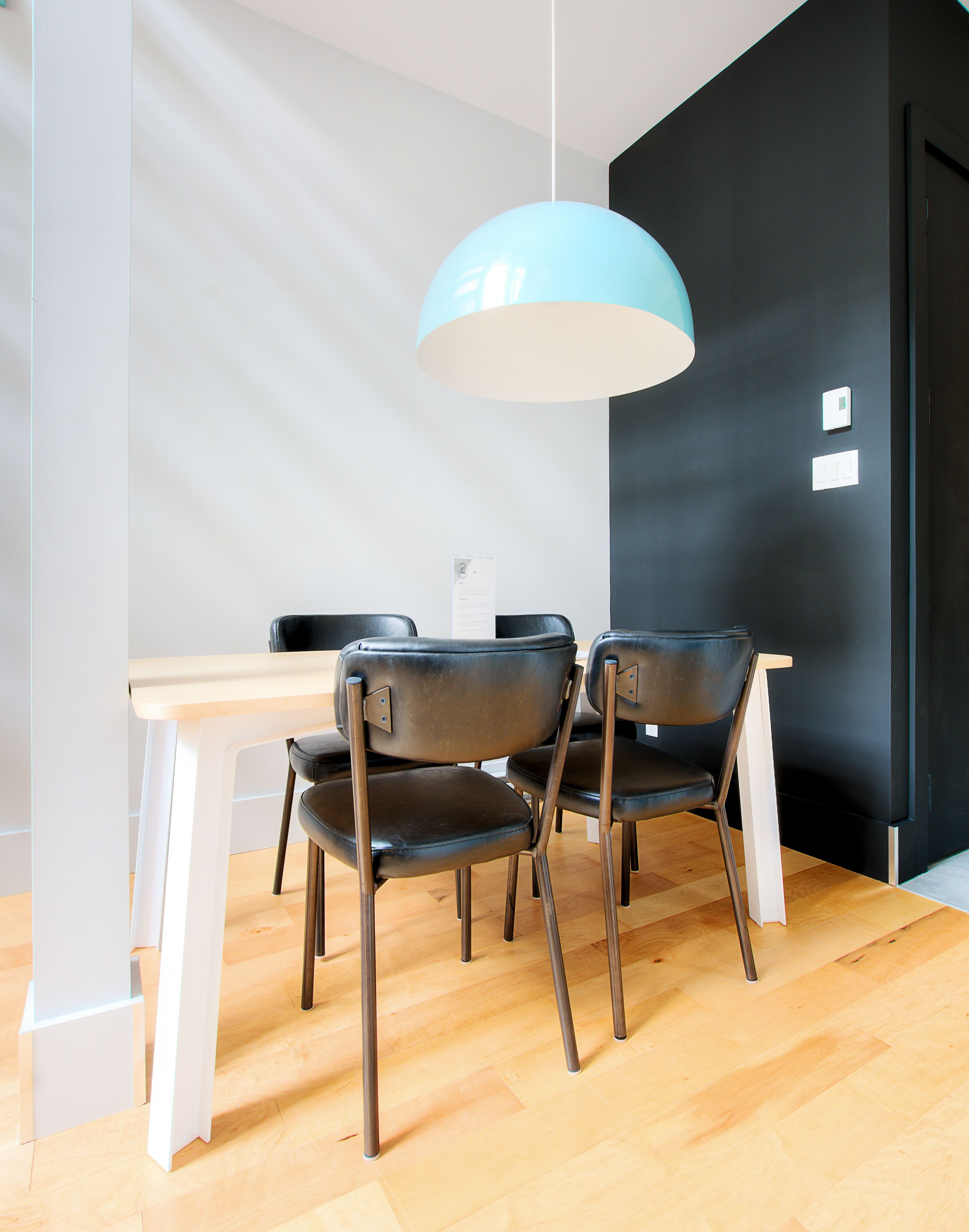 A modern dining area with a wooden table and black chairs, a blue pendant light, and a black accent wall.