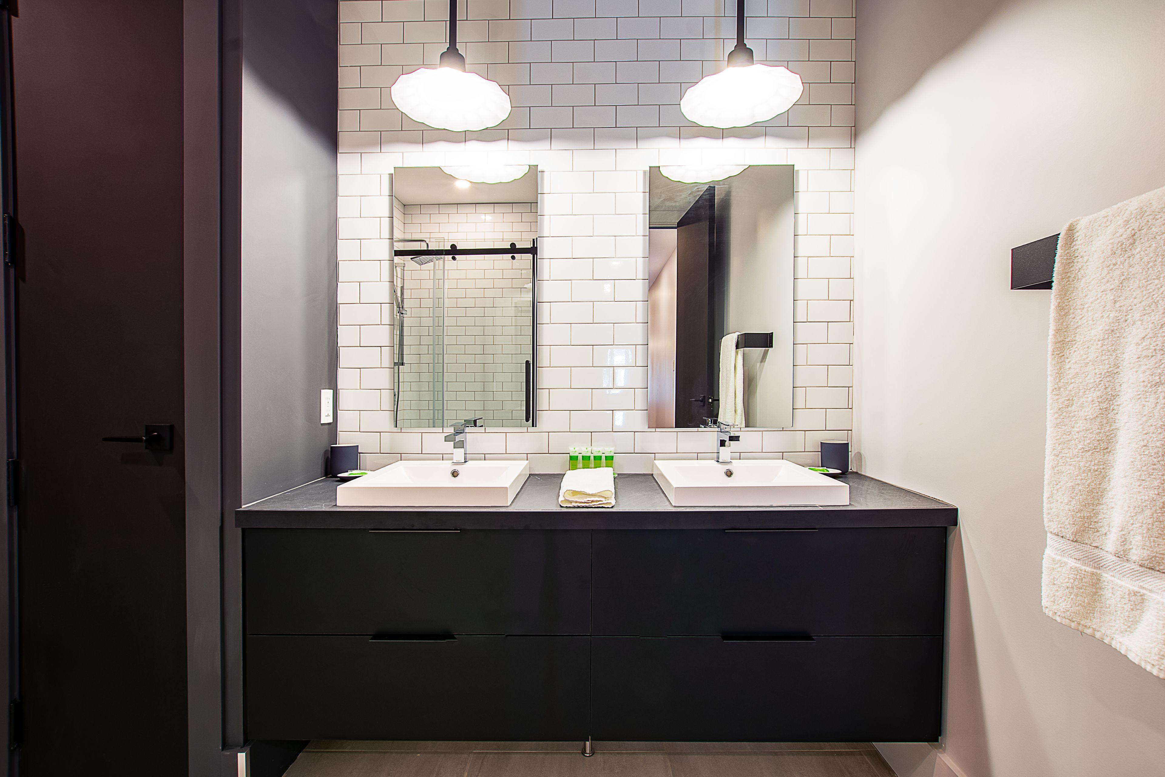 Une salle de bain moderne avec deux vasques, un grand miroir et des meubles de rangement noirs.
