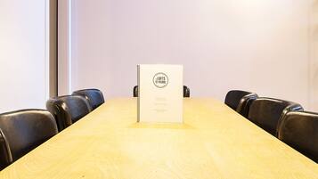 Une salle de conférence avec une table en bois, des chaises en cuir noir, un luminaire suspendu jaune et un tableau blanc posé sur la table.